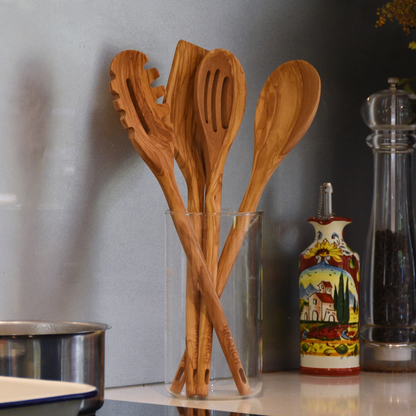 Wooden utensils in a glass holder on a kitchen counter with a decorative bottle in the background.
